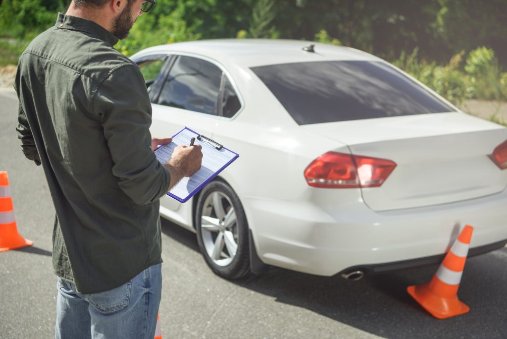 cropped image of man writing something to car insurance on road