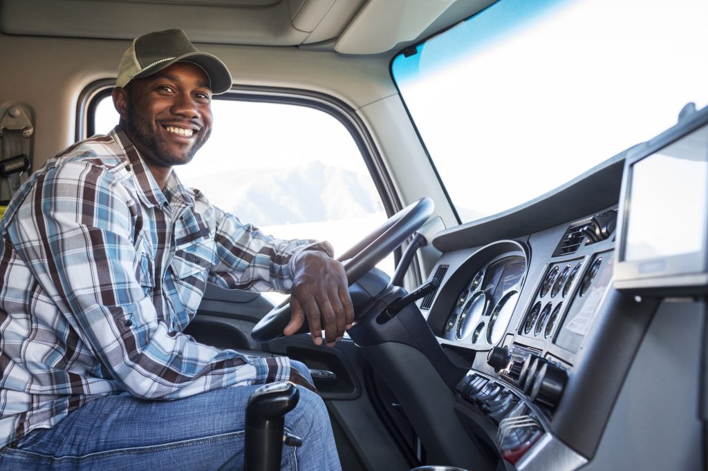 Black man truck driver in the cab of his commercial truck.