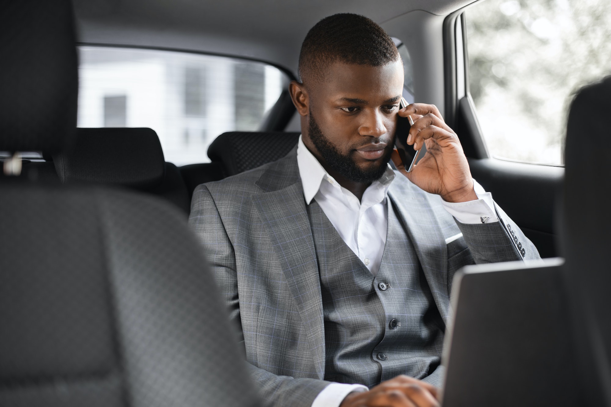 Concentrated black businessman talking on phone in car