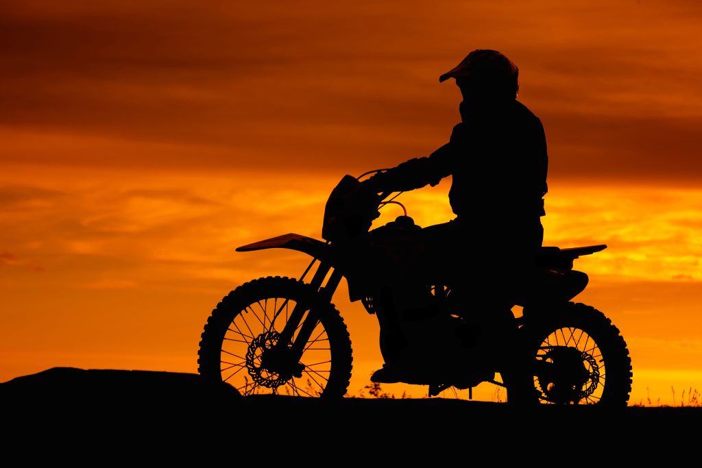 black silhouette of biker with motobike on orange sunset sky background