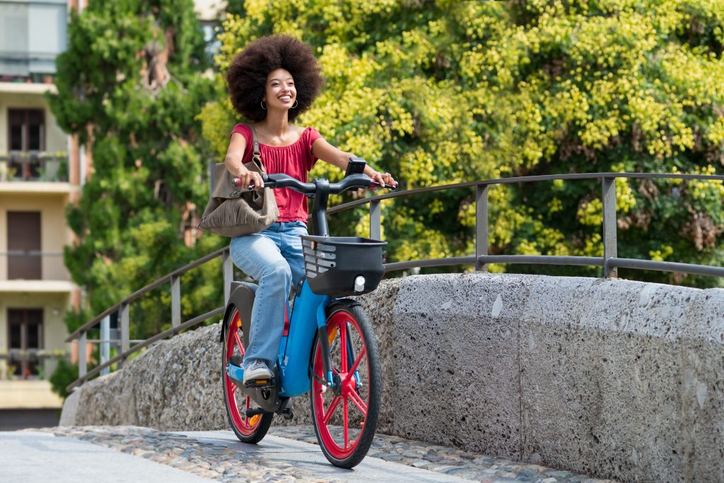 Happy black woman riding electric bicycle on city street bridge