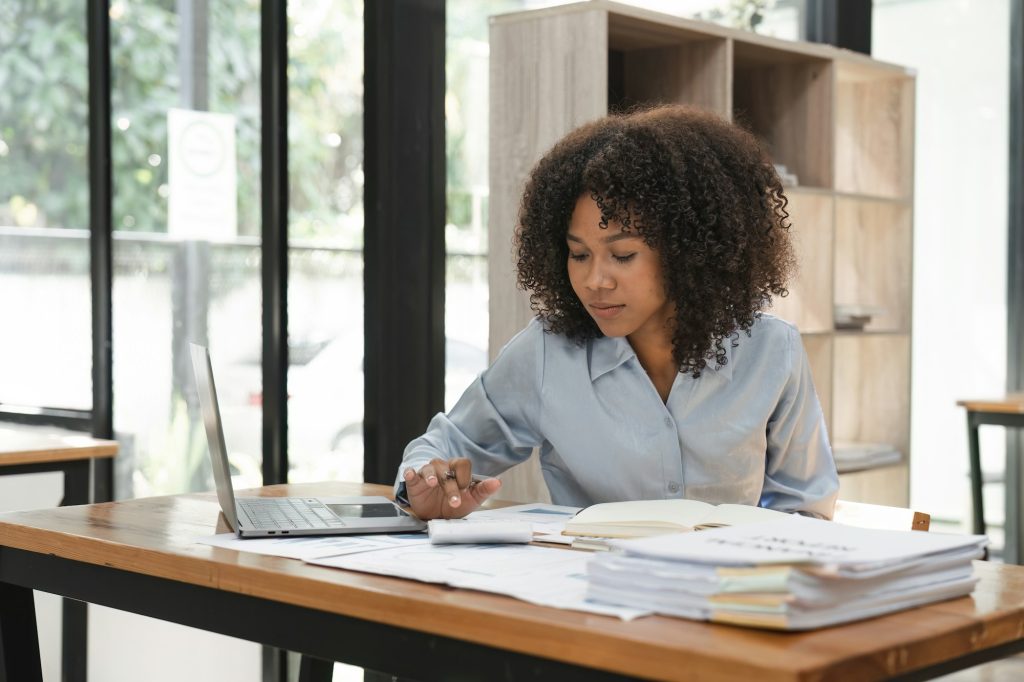 Black business woman calculating finance, money, using calculator, laptop computer at home