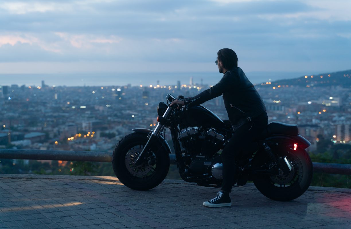 Biker or moto rider after sunset, doing his trip ride with beautiful city views at background