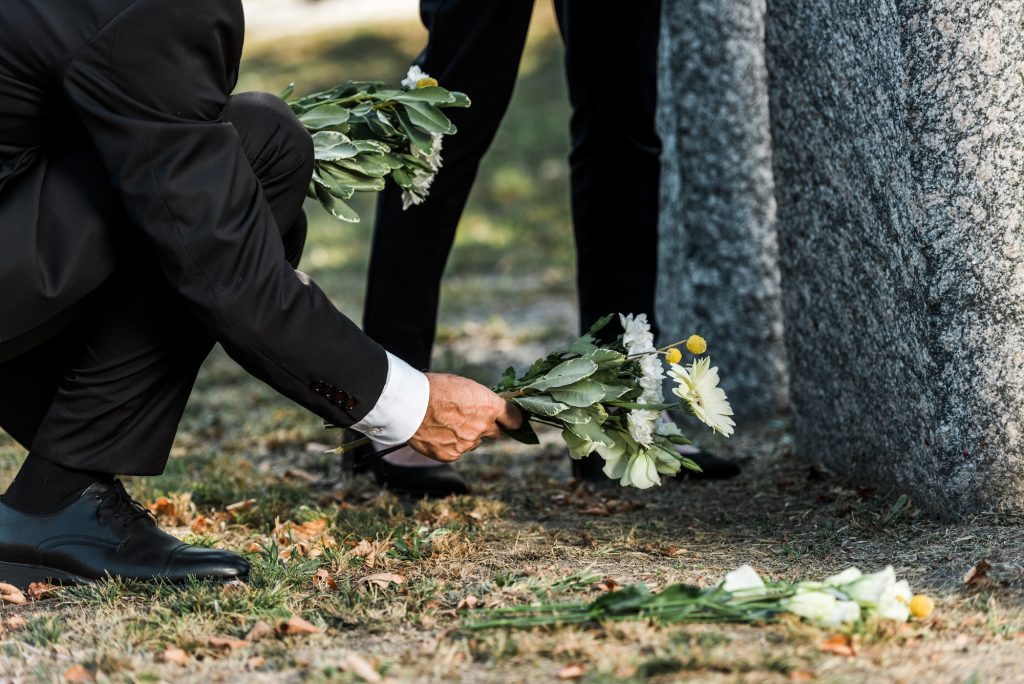 cropped view of senior man putting flowers near tombstones and woman