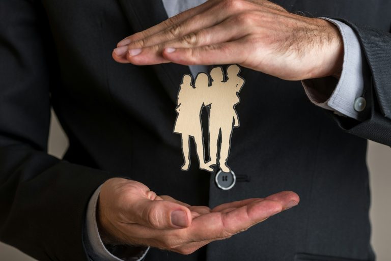 Insurance agent making protecting gesture around a paper cut silhouette of a family