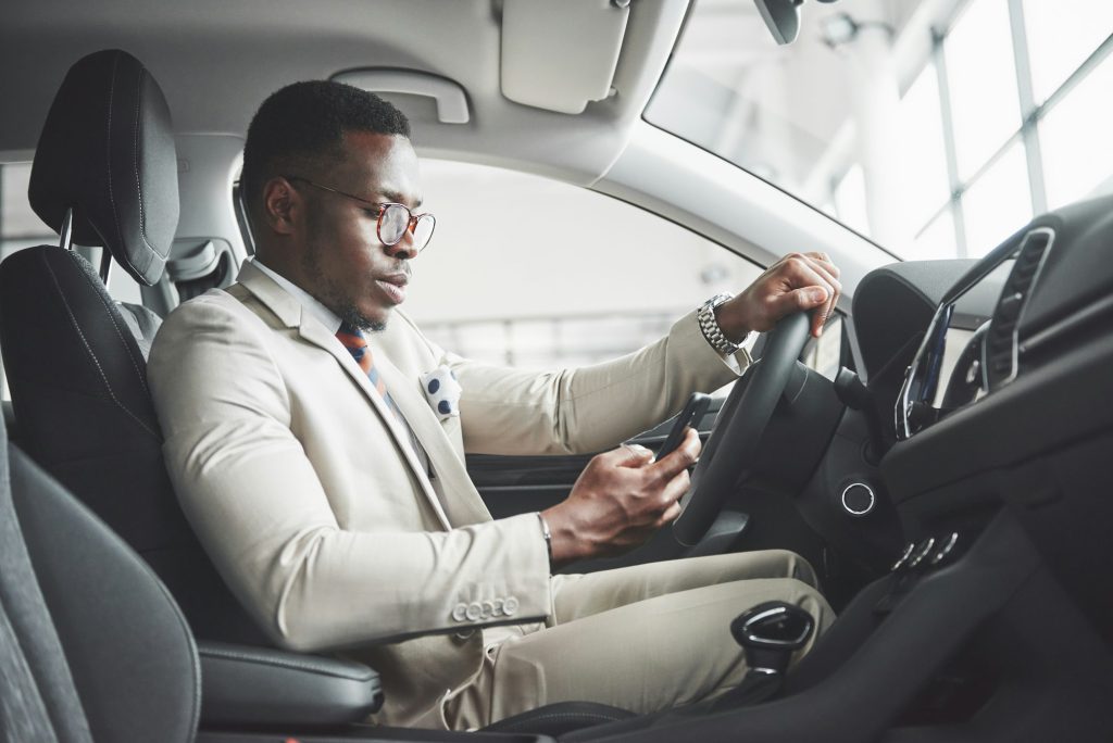 Stylish black businessman sitting behind the wheel of new luxury car. Rich african american man