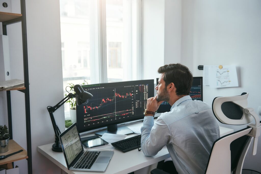 Trading on world markets. Young stock market broker analyzing data and graphs on multiple computer